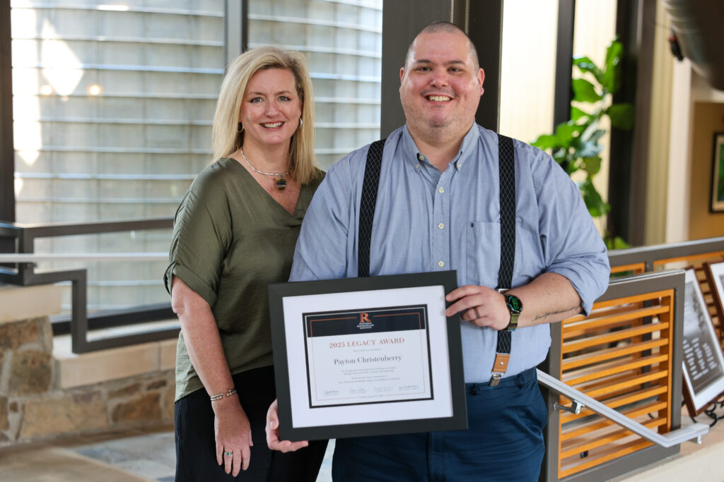 A person and a woman stand together, with the person holding a framed 2025 Legacy Award certificate.